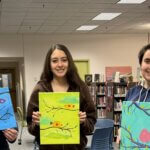 Group of students in the library smiling and holding the paintings they created