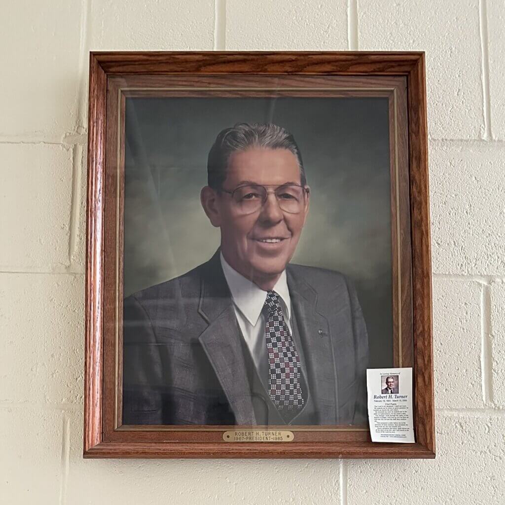 Portrait of Robert H. Turner hanging on a white brick wall.
