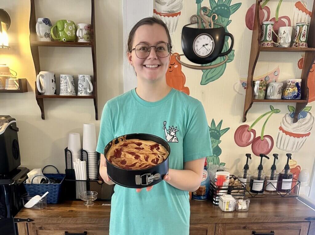 Alum Liberty Tremblay standing in her bakery and holding a cheesecake.