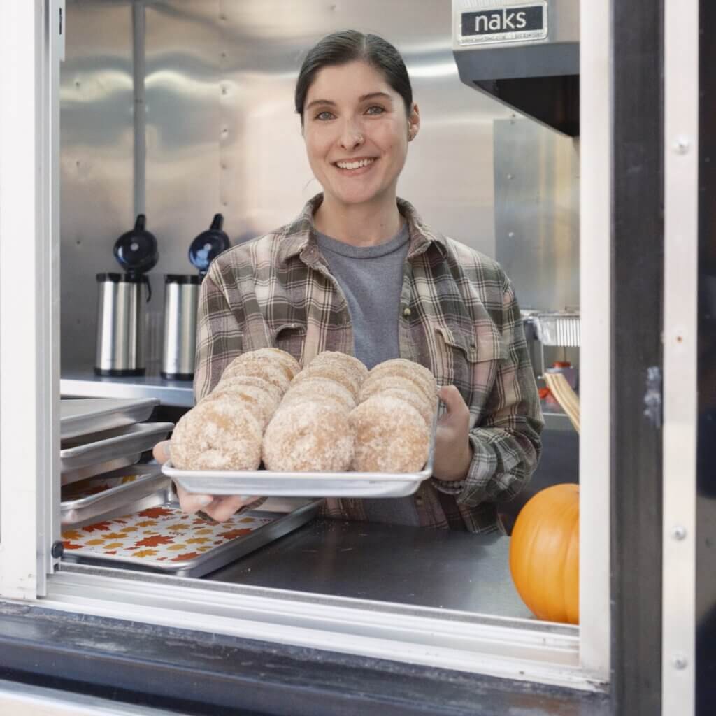Marah Sheehan smiling and holding a tray of pastries while standing in her food truck