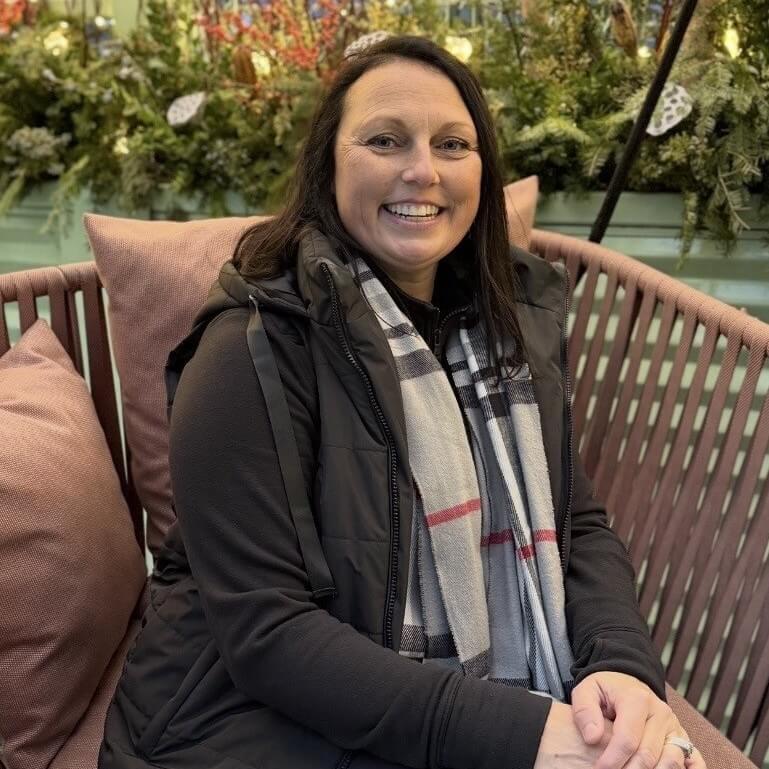 Caroline Drouin sitting in a seat smiling with pretty foliage behind her