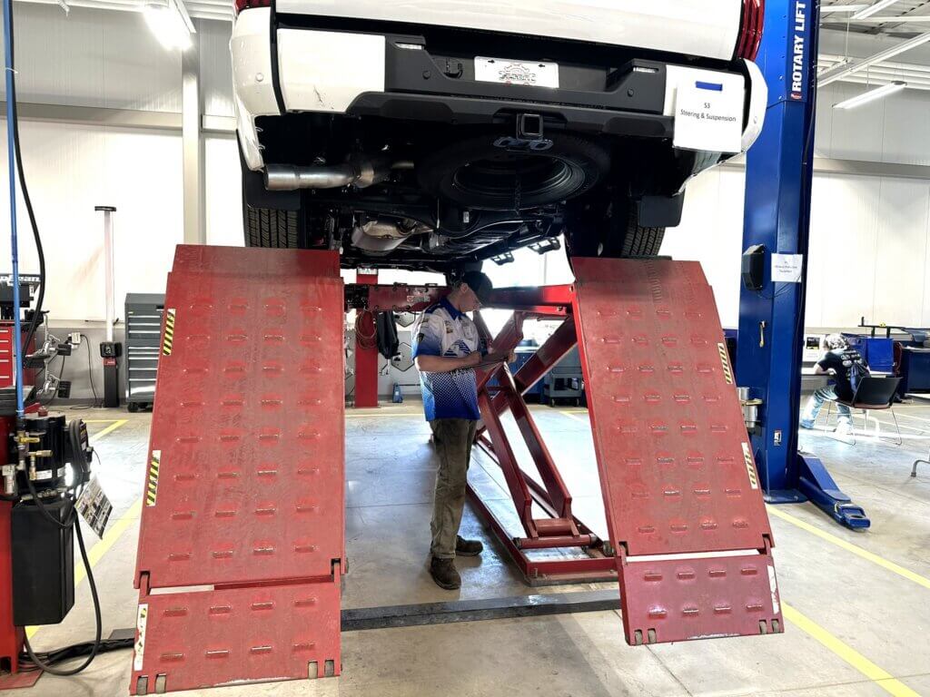 Student standing under a truck up on a lift during SkillsUSA
