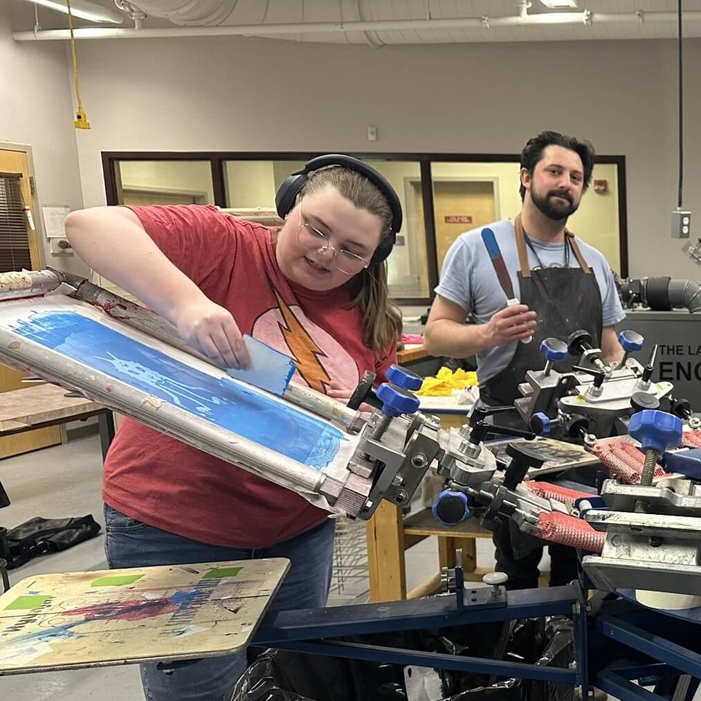 Student screen printing with instructor in background